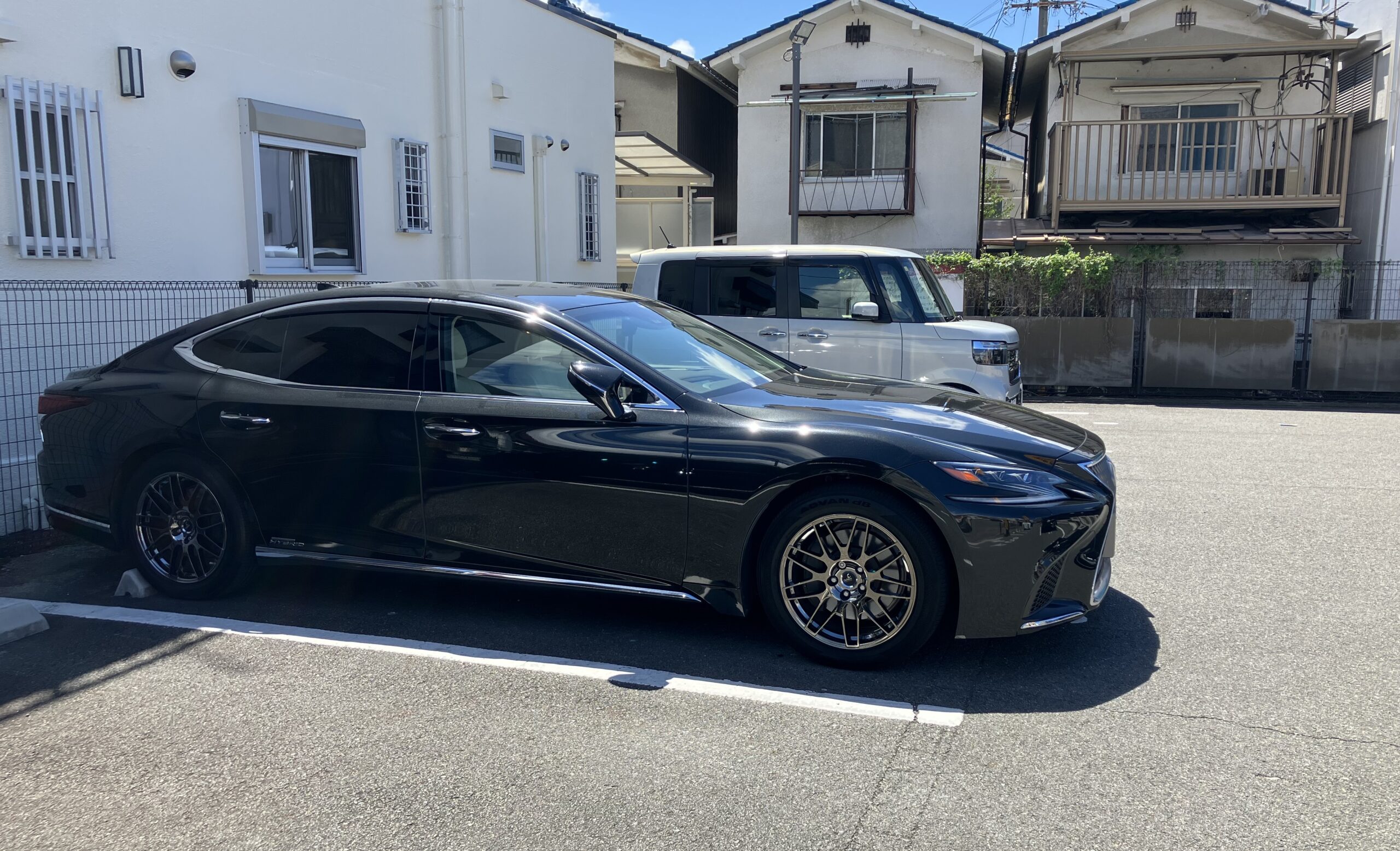 駐車場に停めた黒いレクサスLS500h version Lの右側面とロングボディ